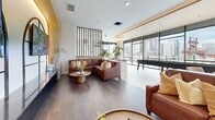 Located at 1050 N Broadway in Denver's Capitol Hill neighborhood, this thoughtfully designed amenity lounge spans a generous single floor, offering an open and versatile communal space. The layout is anchored by large-format light stone tile flooring in the main gathering areas, transitioning to warm hardwood in the lounge zones, creating a clear visual distinction between activity and relaxation areas.

Floor-to-ceiling curtain-wall windows line the perimeter, flooding the interior with abundant natural light and framing panoramic views of the Denver skyline. A full-size billiard table serves as a central focal point of the entertainment zone, surrounded by ample circulation space. Adjacent to it, a long bar-height communal table with modern seating provides a social dining and gathering option.

Slatted wood screens divide zones with architectural elegance, adding warmth and texture without obstructing sightlines. A dedicated lounge area features rich cognac leather seating arranged around a sculptural white coffee table, ideal for casual conversation. The reception-style display wall showcases dual arched TV displays framed in steel, set against ambient backlit cabinetry.

Throughout, curated greenery, pendant lighting, and warm wood accents contribute to a refined yet welcoming atmosphere suitable for both social events and everyday relaxation.