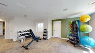 Located at 610 Paradise Ct in Greenwood, Indiana, this dedicated exercise room offers a well-appointed fitness facility designed to support a variety of workout routines. The single-floor space is generously sized, providing ample room to move freely between equipment zones without feeling cramped.

The room features a clean, modern aesthetic with predominantly white walls accented by a bold sage green feature wall that adds a refreshing, energizing touch. Neutral-toned carpet tiles in a herringbone-style layout cover the floor throughout, offering both comfort and durability underfoot. Recessed lighting and a textured ceiling contribute to a bright, functional atmosphere, while multiple windows allow natural light to filter in and provide views of the surrounding outdoor environment.

The fitness area is comprehensively equipped with a diverse selection of workout equipment, including an air resistance bike, rowing machines, a multi-function weight machine, an adjustable workout bench, a full rack of dumbbells, kettlebells, and a dedicated stability and medicine ball storage rack. Two wall-mounted flat-screen TVs are positioned for easy viewing during workouts, and abstract wall art near the feature wall adds a subtle decorative element. A door with glass panels leads to the exterior, further enhancing the sense of openness and airflow within the space.