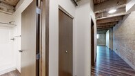 Located at 42–70 Tenth St N in Moorhead, MN, this second-floor 2-bedroom, 2-bathroom unit offers a compelling blend of industrial loft character and modern finishes. The open kitchen is a standout feature, showcasing rich dark-stained cabinetry, stainless steel appliances including a refrigerator, dishwasher, microwave, and range, all set atop warm hardwood-style flooring. Exposed structural beams and a beadboard ceiling add architectural depth and a distinctive industrial charm to the kitchen and living area.

Both bedrooms feature plush carpeting, generous closet space with wide bi-fold doors, and exposed brick accent walls that lend warmth and texture. Large windows allow natural light to fill the rooms while offering views of the surrounding Moorhead streetscape. Baseboard heating runs along the exterior walls, ensuring year-round comfort.

The two bathrooms are well-appointed with dark wood vanities, light countertops, and hardwood-style flooring. One bathroom includes a full tub-shower combination, while the other offers a single vanity with stylish pendant lighting above a large mirror. A hallway connects all rooms, providing a practical and efficient layout throughout this thoughtfully designed urban-style residence.