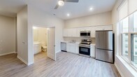 Located at 900 Third St SE in Cedar Rapids, Iowa, this efficiently designed single-floor unit offers a thoughtful layout that maximizes every square foot. The open-concept kitchen and living area is bright and welcoming, finished with light-toned luxury vinyl plank flooring that runs throughout the main space. The kitchen is well-appointed with crisp white shaker-style cabinetry, light countertops, a stainless steel appliance suite including a range, over-the-range microwave, dishwasher, and refrigerator, plus a ceiling fan overhead that adds both comfort and airflow. A large window in the living area frames views of the surrounding Cedar Rapids cityscape, filling the space with natural light. The bedroom is carpeted for warmth and comfort and includes a reach-in closet with built-in shelving, offering practical storage. The bathroom features white cabinetry with a light countertop, an undermount sink with brushed nickel fixtures, and a large wall-mounted mirror illuminated by a modern vanity light bar. Neutral warm beige wall tones, recessed lighting, and clean white trim create a cohesive, modern aesthetic throughout the entire unit.