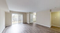 This single-floor unit offers a thoughtfully designed layout that balances open living space with functional private areas. The spacious living room is a highlight, featuring rich hardwood-style flooring, warm neutral-toned walls, and floor-to-ceiling vertical blinds that open to a balcony, flooding the area with natural light and offering views of surrounding greenery. The open flow connects seamlessly to additional rooms, making the space feel airy and expansive.

The kitchen is well-equipped for everyday cooking, featuring warm cherry wood cabinetry that extends to the upper walls for ample storage, a full suite of black appliances including a refrigerator, range, microwave, and dishwasher, along with a functional countertop workspace and light hardwood-style flooring.

The bedrooms provide comfortable retreats, with one room showcasing the same hardwood-style flooring and a built-in closet, while another features soft wall-to-wall carpeting and a bright window that invites natural light. Both rooms maintain the neutral color palette found throughout the unit.

The bathroom is finished with classic white square tile lining the tub and shower surround, accented by a tasteful checkerboard border detail. A wood-toned vanity with a white sink and tile flooring complete the clean, cohesive look of this well-maintained space.