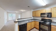 Located at 1201 Aragon Dr in Knightdale, NC, this single-floor, one-bedroom, one-bathroom unit offers a functional and comfortable layout. The combined kitchen and living room creates an open, connected living space. The kitchen is well-appointed with warm honey-toned wood cabinetry, dark granite-style countertops, black appliances including a refrigerator, electric range, built-in microwave, and dishwasher, and durable wood-look flooring. A peninsula counter separates the kitchen from the living area, which transitions to soft carpeting. The living room receives natural light through a large window and offers access to a private balcony. The generously sized primary bedroom features plush carpeting, a ceiling fan, and a dedicated closet. Additional windows throughout bring in abundant natural light and views of surrounding greenery. The full bathroom includes a single-sink vanity with wood cabinetry, a bathtub/shower combination, and wood-look flooring. Textured ceilings are present throughout the unit. The layout is completed by a dedicated closet, offering practical everyday storage.
