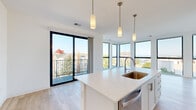 Located at 233 Lake Dr in Racine, Wisconsin, this modern 3-bedroom, 2-bathroom residence offers a thoughtfully designed single-floor layout with clean, contemporary finishes throughout. The open-concept kitchen and living area serves as the heart of the home, showcasing a striking bank of floor-to-ceiling windows that flood the space with natural light and frame sweeping views of Lake Michigan. The kitchen features white shaker cabinetry, stainless steel appliances, quartz countertops, a large center island with a undermount sink, and elegant pendant lighting. Light hardwood flooring runs through the main living areas, complementing the bright, neutral palette. A private balcony is accessible from the living area, extending the indoor-outdoor connection. The three bedrooms are carpeted and well-proportioned, with large windows offering elevated neighborhood and lake views. The primary bedroom includes a sliding barn-style door. Both bathrooms are finished with white vanity cabinetry, quartz countertops, large mirrors, and wood-tone flooring. A dedicated hallway, entrance, and closet round out the functional layout. The overall ambiance is clean, modern, and light-filled, with the waterfront setting adding a distinctive sense of place.
