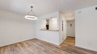 This well-appointed single-floor unit offers three bedrooms and one bathroom within a thoughtfully organized layout. Wood-look plank flooring runs throughout the entire space, providing a warm and cohesive aesthetic from room to room.

The combined living and dining area serves as the heart of the home, featuring a striking circular pendant light fixture and a large window that invites natural light and offers a view to the exterior. The open-concept kitchen connects to the living area via a pass-through counter with a warm wood-toned surface, complemented by decorative pendant lights above and a subway tile backsplash. A built-in shelving nook adds a functional accent to the kitchen area.

The primary bedroom is a comfortable, well-proportioned room equipped with a ceiling fan and light fixture, and benefits from its own dedicated closet space. The additional two bedrooms are clean and bright, each with wood-look flooring. One bedroom notably includes two separate closets, providing generous storage capacity.

The bathroom is finished with classic white hexagonal mosaic floor tile, a full tub and shower combination, and a window that brings in natural ventilation and light. The overall palette throughout the unit is clean and neutral, emphasizing white walls and modern brushed nickel hardware, creating a fresh and move-in-ready environment.
