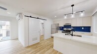 Located at 2330 Grand Ave in San Diego's vibrant Pacific Beach neighborhood, this efficiently designed single-floor studio offers a thoughtfully organized layout across its compact footprint. The combined kitchen and living area serves as the heart of the space, showcasing light wood-look flooring, crisp white walls, and recessed lighting that keep the interior feeling bright and airy. A ceiling fan with integrated lighting adds both comfort and a modern touch. The kitchen is well-appointed with stainless steel appliances — including a full-size refrigerator and electric range — white flat-front cabinetry offering ample storage, white countertops, a peninsula with pendant lighting and an integrated sink, and a striking deep-blue herringbone tile backsplash that adds a bold design accent. A wall-mounted mini-split system provides climate control. Sliding glass doors lead to a private balcony, inviting natural light and outdoor access into the living area. The bathroom features a clean, all-white walk-in shower with matte black fixtures and a built-in shelf, complemented by wood-look flooring. A dedicated laundry area with a stacked washer and dryer unit adds everyday convenience. The overall aesthetic is clean, modern, and functional.