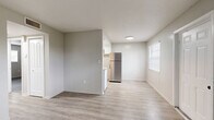 This single-story, 2-bedroom, 1-bathroom unit offers a practical and efficiently designed layout across a compact yet functional footprint. The combined kitchen and living area forms the heart of the space, featuring light wood-look vinyl flooring, neutral gray walls, and white baseboards that create a clean, modern aesthetic throughout. The kitchen is well-equipped with white cabinetry, tile backsplash, a stainless steel refrigerator, a white electric range, and a double-basin sink — all arranged in a U-shaped layout that maximizes counter and storage space. Natural light filters into the living area through a window fitted with blinds, lending the space a bright, open feel. The primary bedroom is a comfortable size, offering a sliding double-door closet with built-in hanging rod, and connects easily to the hallway. The second bedroom also features wood-look flooring, neutral walls, and a window that allows in natural light, making it a versatile space. A dedicated closet provides additional storage. The full bathroom includes a tiled shower-tub combination in white. A connecting hallway links all rooms efficiently, completing this straightforward and move-in-ready layout.