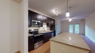 This single-floor unit at Springhouse Apartments offers a thoughtfully designed layout that balances comfort and functionality. The kitchen is a standout feature, equipped with dark espresso cabinetry reaching to the ceiling, stainless steel appliances including a range, microwave, dishwasher, and refrigerator, complemented by granite countertops and a peninsula that opens to the dining and living areas. Pendant and track lighting add a modern touch overhead. The open living area is bright and welcoming, with warm hardwood-style flooring, a ceiling fan, and French doors that invite natural light and provide access to the outdoors. Bedrooms are carpeted for comfort, with at least one featuring a generous walk-in closet complete with wire shelving and a dedicated laundry access panel. Additional bedrooms include ceiling fans and windows that bring in natural light. The bathrooms are finished with warm-toned tile surrounds on the soaking tub and shower combination, granite-topped vanities with dark cabinetry, and hardwood-style flooring. Throughout the unit, neutral tones and clean finishes create a cohesive and move-in-ready atmosphere suited for everyday living.