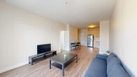 This thoughtfully designed 2-bedroom, 1-bathroom residence is arranged across a single floor, offering a practical and cohesive living experience. The living room is bright and open, featuring light hardwood-style flooring, neutral walls, and large glass sliding doors that invite abundant natural light and provide direct access to an outdoor area with exterior views. The clean, minimalist aesthetic of the space allows for versatile furnishing arrangements.

The kitchen is efficiently laid out with warm-toned cabinetry extending to the ceiling, white tile backsplash, and a full suite of stainless steel appliances including a refrigerator, gas range, microwave, and dishwasher. A compact dining area adjacent to the kitchen provides a convenient space for everyday meals.

The primary bedroom is a well-proportioned room with soft carpeting, a window offering outdoor views, and access to a dedicated closet featuring louvered doors and built-in shelving. The second bedroom is similarly finished with plush carpet and a bright window. The shared bathroom is clean and modern, equipped with a single vanity, large mirror, and a glass-enclosed walk-in shower with tile surround. Overall, the space presents a cohesive, contemporary design with a light, neutral palette throughout.