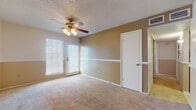 Located at 4405 Summerhill Rd in Texarkana, Texas, this single-floor home offers a practical and comfortable layout with consistent design details carried throughout. The living area welcomes you with a decorative tile entryway that transitions into plush carpeting, two-tone painted walls with a distinctive chair rail, and a ceiling fan with a light fixture. Natural light filters in through blinds-covered windows, creating a bright and airy atmosphere. The open flow connects the living space to a dining area, both finished with the same warm, neutral tones and ceiling fans. The galley-style kitchen is well-equipped with wood cabinetry, light countertops, a stainless steel sink, and black appliances including a range, refrigerator, and dishwasher. A decorative tile backsplash adds visual interest, while light tile flooring keeps the space easy to maintain. The bedrooms continue the carpeted, two-tone wall treatment and are each equipped with ceiling fans. One bedroom features a bay window that brings in generous natural light. The bathrooms are finished with light tile flooring and warm wood vanities. One bathroom includes a tub-shower combination with white tile surround, while another features a vanity with a framed mirror and wall sconce lighting.