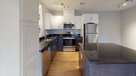 This single-floor residence offers two bedrooms and one bathroom across a thoughtfully designed layout. The open living area is finished with warm wood-style laminate flooring that extends through the main living spaces, complemented by neutral gray walls and crisp white trim throughout. A central hallway connects the key areas of the unit, providing a logical and functional flow.

The kitchen is a standout feature, showcasing a two-tone design with white upper cabinetry and dark lower cabinets, all topped with dark granite countertops. A full suite of stainless steel appliances—including a refrigerator, range, and microwave—adds a modern touch, while track lighting illuminates the space effectively. A kitchen island provides additional counter and prep space.

Both bedrooms are carpeted in a neutral tone, offering a comfortable feel underfoot. Each room benefits from windows that invite natural light and outdoor views. One bedroom includes a built-in closet with a bi-fold door, while a ceiling fan in the living area adds to the unit's practicality.

The bathroom is well-equipped, featuring both a soaking tub and a separate walk-in shower with sliding glass doors and chrome hardware. Large-format tile flooring and a dark-toned vanity round out the space with clean, contemporary style.