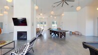Located at 300 Rivermill Dr in Asheville, NC, this single-story community clubhouse is a lively, open-plan gathering space designed for socializing and recreation. The interior is anchored by soaring ceilings adorned with globe pendant lights and oversized ceiling fans, all set above gleaming polished concrete floors that run throughout the space.

The main area is thoughtfully zoned into distinct activity spaces. A cozy lounge area features a modern gas fireplace, a wall-mounted flat-screen TV, and an eclectic mix of colorful seating. Adjacent to it, a games zone offers a pool table and a ping-pong table, providing ample entertainment options. A dining nook with bold, vibrantly upholstered swivel chairs adds a playful touch.

The full kitchen is equipped with stainless steel appliances, including a refrigerator and microwave, gray cabinetry, and a generous island with a rich wood base and light countertop, lined with colorful metal bar stools. Tall windows bathe the kitchen in natural light.

One of the standout features is the wall of industrial-style garage doors that open fully to a balcony overlooking the outdoor pool area, seamlessly blending indoor and outdoor living. A high-top bar table and colorful chairs near the garage doors create an ideal spot to enjoy the view. Throughout the space, the bright white walls and abundant natural light foster an energetic yet welcoming ambiance.