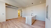 Located at 55 Washington St in East Orange, NJ, this well-appointed 1-bedroom, 1-bathroom unit offers a thoughtfully designed open-concept layout with modern finishes throughout. Light-toned hardwood-style flooring flows seamlessly across the entire space, enhancing its bright, airy feel.

The combined kitchen and living area serves as the heart of the unit. The kitchen features a striking island with a white quartz countertop, wood-toned cabinetry, a matte black faucet, and stainless steel appliances including a gas range, microwave, and refrigerator. A sleek linear pendant light above the island adds a contemporary touch. Recessed lighting and clean white walls keep the space feeling fresh and open.

The living area benefits from large windows that flood the room with natural light and offer views of the surrounding East Orange neighborhood. The bedroom is a comfortable, well-proportioned room with its own generous windows framing bright city views, along with a dedicated closet for storage.

A hallway connects the main living areas to the bathroom, which features a soaking tub with clean white subway-style tile surround. In-unit stacked washer and dryer provide added convenience. The overall design is clean, modern, and move-in ready.
