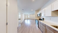 This thoughtfully designed 2-bedroom, 2-bathroom residence offers a functional single-level layout with a clean, contemporary aesthetic. The open-concept kitchen and living area serves as the heart of the home, with light wood-tone flooring flowing throughout. The kitchen is equipped with stainless steel appliances—including a range, microwave, refrigerator, and dishwasher—paired with two-tone cabinetry featuring white upper cabinets and warm wood-toned lower cabinets, complemented by light quartz countertops. The living area extends toward a glass door and windows that provide outdoor views and ample natural light, with access to a balcony. Both bedrooms are carpeted and receive natural light through sizeable windows; one bedroom features a ceiling fan and an en-suite bathroom with a dual-sink vanity, dark wood cabinetry, and a large mirror. The second bathroom mirrors the same modern finishes. Two dedicated closets—including a spacious walk-in with wire shelving—provide generous storage. Recessed lighting throughout the common areas and a neutral color palette give the space a bright, cohesive feel.