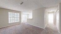 This single-floor residence offers a thoughtfully laid-out floor plan with a bright, open-concept living and dining area at its core. The living space is finished with plush wall-to-wall carpeting and neutral beige tones, creating a clean and versatile backdrop. Large windows allow natural light to fill the room, offering views of the surrounding greenery and an adjacent balcony or patio area. A textured ceiling adds classic detail overhead, while a ceiling-mounted HVAC vent ensures year-round comfort.

The kitchen features a galley-style layout with light wood cabinetry, white appliances including an electric range, refrigerator, and dishwasher, complemented by a tile backsplash and durable tile flooring. A pass-through opening connects the kitchen to the dining area, where a pendant light fixture hangs overhead, enhancing the sense of continuity between spaces.

The bedrooms are generously proportioned, each with soft carpeting, neutral walls, and large windows that bring in ample natural light. Closet access is conveniently located within the bedrooms. The bathroom is finished with tile flooring, a full soaking tub and shower combination, a vanity with a white countertop, and a wall-mounted mirror, all presented in a clean, understated palette.