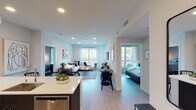 This contemporary single-floor residence showcases a thoughtfully designed open-concept layout that seamlessly connects the kitchen, dining, and living areas into one cohesive, light-filled space. The kitchen is appointed with dark espresso cabinetry, stainless steel appliances including a gas range and dishwasher, a white quartz peninsula with bar seating, and a classic white subway tile backsplash. Light wood-tone flooring runs throughout the main living areas, complementing the clean white walls and recessed lighting overhead. The living room offers generous natural light through large windows with outdoor views, and features a wall-mounted TV and ample space for relaxed seating. A dedicated dining area with a round table sits conveniently between the kitchen and living space. The two bedrooms are well-proportioned, each with large windows that invite natural light and outdoor scenery. The primary bedroom includes a spacious closet, while the second bedroom offers room for a workspace alongside the bed. Both bathrooms are finished with dark vanity cabinetry, white quartz countertops, and tub-shower combinations with white tile surrounds. The overall ambiance is modern, clean, and functional, creating a comfortable and stylish living environment.