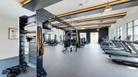 Located at 2175 Easton Loop in Kissimmee, FL, this well-appointed fitness center offers a generously sized, single-floor exercise space designed to support a full spectrum of workout routines. The interior is defined by soaring ceilings accented with warm wood beams and slat detailing, creating an inviting yet energizing atmosphere throughout the facility.

The cardio zone features a long row of treadmills and elliptical machines from True Fitness, along with stationary bikes, all positioned along large floor-to-ceiling windows that flood the space with natural light and offer views of the surrounding palm-lined landscape. A dedicated TRX functional training station anchors one end of the room, complemented by an open hardwood-floored area ideal for stretching or group exercise.

The strength training section is equally well-equipped, housing a full rack of dumbbells, multiple Inspire Fitness cable and resistance machines, adjustable benches, and a dedicated free weights platform. Full-length mirrors line portions of the walls, enhancing both the sense of space and functional use during training. Ceiling fans and pendant lighting provide comfort and ambiance, while durable rubber and speckled flooring throughout ensures safety and performance. The overall design balances modern aesthetics with practical functionality.