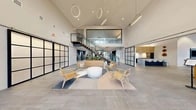 Located at 10999 SE 37th Ave in Milwaukie, Oregon, this thoughtfully designed two-story amenity space offers a generous and versatile environment spread across two floors. The main level sets an impressive tone with a soaring vaulted ceiling in the central lobby, adorned with sculptural ring pendant lights and large steel-framed windows that flood the space with natural light. Large-format tile flooring, an open seating arrangement, and a floating staircase with glass-panel railings anchor the dramatic entry. Adjacent to the lobby, a stylish lounge features a statement stacked-stone fireplace with a built-in TV, high ceilings, and comfortable seating — ideal for relaxed gatherings. A fully equipped kitchen bar area showcases navy cabinetry, granite countertops, a white subway tile backsplash, and seating for multiple guests, complemented by a separate dining area bathed in natural light through floor-to-ceiling steel-framed windows. The upper level provides dedicated coworking and focus areas, with a mix of open-plan workstations, lounge seating, and a glass-partitioned private workspace. Textured carpet, vaulted ceilings, and abundant natural light create a productive yet comfortable atmosphere. Throughout, the design blends modern industrial elements with warm wood accents, delivering a cohesive and inviting community space.