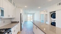 This thoughtfully designed 2-bedroom, 1-bathroom residence offers a bright and contemporary living experience across a single floor. Light-toned hardwood-style flooring flows seamlessly throughout, enhancing the open and airy feel of the space.

The kitchen is a standout feature, showcasing white shaker cabinetry that extends to the ceiling with glass-front upper cabinets, a subtle tile backsplash, dark quartz countertops, a center island for additional prep and seating space, and a full suite of stainless steel appliances including a gas range, dishwasher, and French door refrigerator.

The kitchen opens directly into a spacious living area, creating an ideal open-concept layout. Recessed lighting throughout ensures consistent illumination. The living area benefits from a large sliding glass door that floods the room with natural light and provides outdoor views.

Both bedrooms are generously sized and feature sliding glass doors with views of the surrounding community, including lush landscaping and palm trees. Each bedroom is served by its own walk-in closet outfitted with wire shelving systems for organized storage.

The bathroom is clean and modern, featuring a white vanity with dark quartz countertops, a framed mirror, and a shower. The overall design palette — crisp whites, neutral tones, and natural wood-look flooring — creates a cohesive, contemporary ambiance throughout.