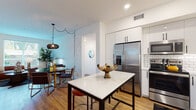 Located at 22151 Clarendon St in Woodland Hills, Los Angeles, this single-story 2-bedroom residence combines modern design with practical functionality. The open-concept kitchen is a standout feature, equipped with stainless steel appliances including a French door refrigerator, range, microwave, and dishwasher. White shaker cabinetry with matte black hardware lines the walls above a classic white subway tile backsplash, while a central island with a white quartz countertop provides additional prep space and casual seating. Warm wood-tone flooring flows throughout the main living areas, connecting the kitchen seamlessly to a dining nook and living room.

The living room offers a comfortable, well-proportioned layout with clean white walls suited for displaying artwork. Both bedrooms feature plush carpeting and ample natural light. The primary bathroom includes a glass-enclosed shower, a soaking tub, and wood-look flooring, while the second bathroom offers a tub-shower combo and a backlit vanity mirror. A dedicated in-unit laundry closet with a stacked washer and dryer adds significant convenience. The overall aesthetic is clean, contemporary, and thoughtfully designed.