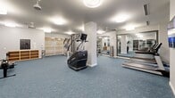 This expansive 2,090 square foot fitness center is a testament to modern exercise facility design. The space is divided into multiple zones, each dedicated to different workout styles. A cardio area features treadmills and stationary bikes, while a separate strength training section is equipped with weight machines and free weights. The facility boasts a variety of exercise equipment, including ellipticals, rowing machines, and multipurpose strength training stations.

Large windows allow natural light to flood the space, creating an open and inviting atmosphere. The bright white walls and ceiling, coupled with the soft blue carpeting, contribute to a clean and calming environment. Strategically placed mirrors and glass partitions enhance the sense of spaciousness and allow for proper form monitoring during workouts.

The center is outfitted with modern amenities, including wall-mounted televisions, water stations, and sanitizing areas. The layout is thoughtfully designed to maximize floor space while ensuring easy navigation between different workout zones. High ceilings with recessed lighting fixtures provide even illumination throughout the facility.

This well-equipped fitness center offers a comprehensive workout experience, catering to various fitness levels and preferences in a bright, spacious, and meticulously maintained environment.