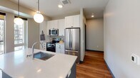 Located at 5075 Wayzata Blvd in Golden Valley, MN, this single-floor unit features a thoughtfully designed contemporary interior with consistent finishes throughout. The open-concept living area is anchored by warm hardwood-style flooring and a bank of large windows that frame views of the surrounding urban streetscape, filling the space with abundant natural light. Dark-framed door and window trim contrast cleanly against neutral warm-toned walls, creating a modern, cohesive aesthetic carried throughout every room.

The kitchen is well-equipped with stainless steel appliances, including a refrigerator, electric range, and built-in microwave. White shaker-style cabinetry reaches the ceiling for ample storage, complemented by a herringbone tile backsplash and a quartz-topped island with an undermount sink and pendant lighting above.

Bedrooms feature plush carpeting, individual windows with exterior views, and direct access to hallways connecting to bathroom facilities. The primary bathroom offers a double-sink vanity with quartz countertops, a wood-framed mirror, hardwood-style flooring, and a soaking tub with shower. A secondary full bathroom provides similar quality finishes in a more compact layout, ensuring comfort and functionality throughout the residence.