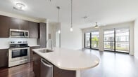 Located on South Howard Avenue in Tampa's desirable 33629 corridor, this single-floor residence offers a thoughtfully designed open-concept layout with contemporary finishes throughout. The kitchen serves as the centerpiece of the living area, featuring dark espresso cabinetry, stainless steel appliances including a refrigerator, range, microwave, and dishwasher, and a curved white quartz island with an integrated sink. Dual pendant lights hang above the island, adding a refined touch, while rich dark hardwood flooring extends throughout the main living and kitchen areas. The living space opens toward floor-to-ceiling glass doors that lead to a balcony, allowing natural light to fill the room, complemented by a ceiling fan overhead.

The bedrooms are carpeted for comfort, each featuring ceiling fans and windows that bring in natural light and outdoor views. One bedroom includes access to a generously sized walk-in closet outfitted with multi-tiered wire shelving and hanging rods. Two bathrooms serve the unit: one with a soaking tub and tiled surround, and another with a glass-enclosed walk-in shower. Both feature light tile flooring, white quartz vanities, and wood-toned cabinetry, maintaining a clean and cohesive modern aesthetic throughout.