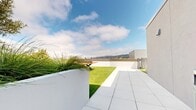 Located at 2108 Berkeley Way in Berkeley, CA, this rooftop amenity deck offers a thoughtfully designed outdoor retreat above the urban streetscape. The space is defined by a clean, modern aesthetic characterized by crisp white parapet walls, large-format porcelain tile paving, and generous stretches of lush artificial turf that lend a park-like feel to the elevated setting.

Multiple distinct zones encourage a variety of uses. A spacious lounge area is furnished with plush, cushioned seating in muted green and neutral tones, accented by warm teak side tables and a low coffee table — ideal for relaxed gatherings or quiet outdoor moments. Concrete planters overflow with ornamental grasses, adding organic texture and a layer of privacy throughout the deck.

A dedicated recreation area features a striking wood-and-steel ping-pong table set directly on the turf, providing an active counterpoint to the lounge. An elongated turf corridor runs along one side of the building, offering additional open-air space framed by the building's architectural forms.

Panoramic views of the Berkeley Hills serve as a dramatic natural backdrop, visible from multiple vantage points across the deck. Under open skies and abundant California sunlight, this rooftop space presents an inviting, well-appointed environment suited for community gathering, recreation, and relaxation.