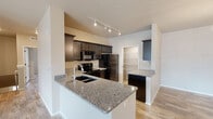 This single-floor residence offers a thoughtfully designed layout with modern finishes and practical features throughout. The kitchen serves as a functional centerpiece, equipped with dark espresso cabinetry, granite countertops, black stainless steel appliances including a range, microwave, and refrigerator, and a peninsula with an integrated sink — ideal for both cooking and casual dining. Track lighting overhead enhances the workspace.

The dining area is bright and welcoming, featuring a stylish orb pendant light and a large window that brings in natural light. Light wood-tone flooring runs consistently throughout the home, creating a cohesive and clean aesthetic.

The bedrooms are generously sized, with vaulted ceilings in the primary bedroom adding an airy sense of volume. Each bedroom benefits from walk-in closets outfitted with wire shelving systems, offering excellent storage capacity. The bathrooms are clean and functional, featuring dark wood vanities, light stone-look countertops, single-basin sinks, and large mirrors.

A dedicated laundry area houses a full-size washer and dryer with additional wire shelving above. The home also includes a spacious walk-in storage closet with multi-tiered wire shelving. Neutral wall tones and consistent wood-look flooring throughout create a calm, move-in-ready environment.