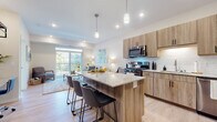 This thoughtfully designed single-floor residence showcases a seamless open-concept layout connecting the kitchen, dining, and living areas. The kitchen is a standout feature, equipped with light wood cabinetry, a classic white subway tile backsplash, granite countertops, and a full suite of stainless steel appliances including a gas range, microwave, dishwasher, and refrigerator. A generously sized kitchen island with seating for multiple guests serves as both a functional workspace and a social hub, illuminated by stylish pendant lighting overhead. Light wood-tone flooring flows throughout the main living areas, contributing to a warm, cohesive aesthetic. The living room is bright and inviting, with large sliding glass doors opening to a private balcony that offers pleasant outdoor views and an abundance of natural light. The bedroom is spacious and carpeted, featuring a ceiling fan, ample natural light from a large window, and a calming, neutral color palette. The bathroom is finished with granite countertops, wood-toned cabinetry, and light flooring consistent with the rest of the home. Throughout the space, clean lines, recessed lighting, and a neutral tone create a contemporary and comfortable atmosphere.