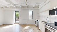 Located at 1045 W Lawrence Ave in Chicago's vibrant Uptown neighborhood, this single-floor unit blends industrial character with contemporary finishes throughout. Polished concrete floors extend across all areas, complementing the exposed structural beams and utility conduits painted crisp white overhead, lending the space an open, loft-like aesthetic.

The kitchen is thoughtfully designed with white cabinetry reaching toward the ceiling, white subway tile backsplash, open shelving, and a full suite of stainless steel appliances including a range, microwave, dishwasher, and refrigerator. In-unit laundry is conveniently integrated into the kitchen area. Track lighting illuminates the space efficiently throughout.

The living and sleeping areas are bright and airy, with large black-framed windows drawing in natural light and offering views of the surrounding urban neighborhood. The clean white walls provide a versatile backdrop, while the exposed ceiling structure adds industrial depth and character.

The bathroom continues the minimalist aesthetic with a floating white vanity, mirrored medicine cabinet, and a walk-in shower with chrome fixtures, all set against white walls and matching concrete flooring.

A standout feature of this unit is the private outdoor terrace, enclosed by modern metal railings and overlooking a lush canopy of trees — a rare urban retreat offering open sky views in the heart of Chicago.