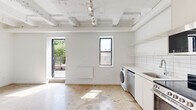 Located at 1045 W Lawrence Ave in Chicago's vibrant Uptown neighborhood, this single-floor unit blends industrial character with contemporary finishes throughout. Polished concrete floors extend across all areas, complementing the exposed structural beams and utility conduits painted crisp white overhead, lending the space an open, loft-like aesthetic.

The kitchen is thoughtfully designed with white cabinetry reaching toward the ceiling, white subway tile backsplash, open shelving, and a full suite of stainless steel appliances including a range, microwave, dishwasher, and refrigerator. In-unit laundry is conveniently integrated into the kitchen area. Track lighting illuminates the space efficiently throughout.

The living and sleeping areas are bright and airy, with large black-framed windows drawing in natural light and offering views of the surrounding urban neighborhood. The clean white walls provide a versatile backdrop, while the exposed ceiling structure adds industrial depth and character.

The bathroom continues the minimalist aesthetic with a floating white vanity, mirrored medicine cabinet, and a walk-in shower with chrome fixtures, all set against white walls and matching concrete flooring.

A standout feature of this unit is the private outdoor terrace, enclosed by modern metal railings and overlooking a lush canopy of trees — a rare urban retreat offering open sky views in the heart of Chicago.