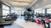 The fitness center at Brookhaven Lofts is a thoughtfully designed amenity space that provides residents with a comprehensive workout environment. The facility is accessed through striking steel-framed glass doors, offering a transparent view into the space and lending it a contemporary, industrial-modern aesthetic that complements the loft-style architecture of the community.

The interior is organized to accommodate a wide range of fitness activities. A dedicated cardio zone lines one wall and features multiple treadmills, including Landice and T1000 models, along with elliptical trainers, providing ample options for aerobic exercise. Strength training is equally well-represented, with multi-station cable machines positioned near large, multi-pane windows that allow generous natural light to fill the space.

A free-weight section houses a full rack of dumbbells alongside adjustable benches, while a functional training area is stocked with medicine balls, stability balls in various sizes, and additional accessories. Floor-to-ceiling mirrors span one wall, visually expanding the space and supporting proper form during workouts. Mounted flat-screen televisions are positioned throughout for entertainment.

The flooring features a two-tone design in contrasting light and dark sections, clearly delineating workout zones. Recessed lighting and linear pendant fixtures ensure consistent illumination throughout, contributing to the clean, energetic ambiance of the facility.
