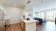 Located at 1009 S 10th St in Sheboygan, WI, this well-appointed one-bedroom, one-bathroom unit offers a thoughtfully designed layout across a single floor. The open-concept kitchen and living area serves as the heart of the unit, where a sleek peninsula with a white quartz countertop and bar seating connects the kitchen to the living space. The kitchen features stainless steel appliances, including a full-size refrigerator and range, light wood cabinetry paired with white upper cabinets, and a modern pendant light fixture overhead. Warm luxury vinyl plank flooring runs throughout the main living areas, adding a cohesive and contemporary feel. The living room is bathed in natural light from large windows that frame outdoor views of the surrounding Sheboygan cityscape. The bedroom is a comfortable retreat with plush carpet, a walk-in closet, and its own set of large windows continuing the bright, airy ambiance. The full bathroom is finished with clean white walls, wood-toned cabinetry, and accessible grab bar features. Additional conveniences include two closets and an in-unit laundry area, rounding out this efficient and modern living space.