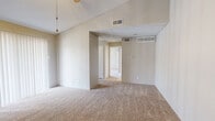 This single-floor, one-bedroom, one-bathroom unit offers a functional and efficient layout with a neutral, move-in-ready aesthetic throughout. The combined kitchen and living room serves as the heart of the home, featuring vaulted ceilings that lend a sense of openness well beyond the unit's compact footprint. A ceiling fan with a light fixture enhances comfort in this shared space, which also benefits from a large sliding glass door covered by vertical blinds, allowing for generous natural light and outdoor access. The entry area continues the vaulted ceiling design, creating an airy first impression upon arrival. Soft, neutral-toned carpet flows throughout the living areas and bedroom, complementing the light, warm wall tones present across the unit. The spacious primary bedroom offers its own ceiling fan, a window with natural light, and ample room for furnishings. Two closets provide excellent storage capacity, including what appears to be a walk-in closet with built-in shelving on both sides. The bathroom features wood-look flooring, a shower-tub combination, and clean white fixtures. Additional practical spaces include a pantry and a dedicated utility room. The overall ambiance is clean, bright, and neutral, offering a versatile canvas for personalization.