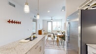 This thoughtfully designed one-bedroom, one-bathroom residence offers an efficient and functional single-floor layout that maximizes every square foot. The open-concept living area seamlessly integrates the kitchen, dining, and living spaces, creating a bright and airy atmosphere filled with natural light from large windows and a glass-panel exterior door with outdoor views of surrounding greenery.

The kitchen is outfitted with crisp white shaker cabinetry, granite countertops, a classic subway tile backsplash, stainless steel appliances including a refrigerator, dishwasher, and range, and a central island that provides additional prep and counter space. Stylish brass pendant lighting adds a warm accent overhead. The dining area accommodates a full-sized table, while the living area features a ceiling fan for added comfort.

The bedroom is a quiet retreat, highlighted by a botanical-print accent wall, a large window with outdoor tree views, and light wood flooring that runs throughout the unit. A generously sized walk-in closet offers wire shelving along multiple walls for organized storage. The full bathroom includes a granite-topped vanity with white cabinetry, a combination tub and shower, and wood-look flooring. A dedicated laundry area with washer and dryer connections and wall shelving rounds out this well-appointed residence.