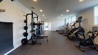 The fitness center at The Grand at Saddle Brook in Saddle Brook, NJ, is a thoughtfully designed single-floor facility that provides residents with a comprehensive workout environment. The space features durable rubber flooring throughout, recessed lighting set into smooth ceilings with crown molding details, and neutral white walls that contribute to a clean, focused atmosphere.

The cardio zone is well-appointed with multiple treadmills by Star Trac, StairMaster steppers, LessMills cycling bikes, and elliptical machines, offering a variety of options for cardiovascular training. Natural light filters in through windows along one wall, adding brightness to the space.

The strength and functional training area includes a heavy-duty power rack fully loaded with Olympic weight plates, adjustable benches, a dumbbell rack, and a TRX suspension system mounted to a dedicated rig. An organized storage shelf keeps medicine balls and kettlebells easily accessible.

A glass sliding door connects the fitness center to an adjacent common area, enhancing the sense of openness. The layout is efficiently arranged to maximize usable floor space while maintaining clear circulation paths, making it a practical and well-rounded amenity for residents of all fitness levels.