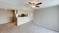 This single-floor residence offers a practical and cohesive layout finished in warm neutral tones throughout. The open living area is carpeted and anchored by a ceiling fan with a light fixture, creating a comfortable and well-ventilated space. A half-wall partition connects the living area to the kitchen, which features stainless steel appliances including a refrigerator, range, and microwave, complemented by dark granite-style countertops, white cabinetry, and wood-look flooring that adds warmth underfoot. The galley-style kitchen layout maximizes efficiency within the space.

The bedrooms continue the neutral carpet flooring and are each equipped with ceiling fans for added comfort. Multiple windows dressed with horizontal blinds allow natural light to fill the rooms, enhancing the open feel. Two bathrooms are present, each featuring a full tub and shower combination with chrome fixtures and a window with blinds that introduces additional natural light. One bathroom includes an open shelving unit for convenient storage. White trim and baseboards provide clean contrast against the taupe walls throughout, giving the entire residence a tidy, move-in-ready appearance.