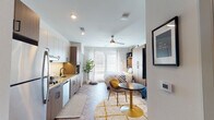 Located at 400–430 N Lincoln Ave in Urbana, Illinois, this thoughtfully designed studio offers a cohesive open-plan layout that seamlessly integrates living, sleeping, and dining functions within a single, well-organized space. The herringbone-patterned flooring flows throughout, lending a refined, contemporary aesthetic that unifies every zone of the unit.

The kitchen is outfitted with two-tone cabinetry—white uppers paired with warm wood lowers—complemented by granite countertops, a subway tile backsplash, a matte black faucet, and stainless steel appliances including a dishwasher and built-in microwave. A ceiling fan overhead promotes airflow across the open living area, which benefits from a large window that draws in natural light.

A substantial wood-toned wardrobe and shelving unit anchors the sleeping area, providing generous storage alongside open display shelving above. A wall-mounted television and a compact sofa define a relaxed lounge area, while a bistro-style table and chairs offer a dedicated dining spot.

The full bathroom continues the herringbone flooring detail and includes a granite-topped vanity with warm wood cabinetry, a bathtub with shower, and crisp white walls. An in-unit stacked washer and dryer adds everyday convenience, completing this efficient and modern single-floor studio.