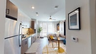 Located at 400–430 N Lincoln Ave in Urbana, Illinois, this thoughtfully designed studio offers a cohesive open-plan layout that seamlessly integrates living, sleeping, and dining functions within a single, well-organized space. The herringbone-patterned flooring flows throughout, lending a refined, contemporary aesthetic that unifies every zone of the unit.

The kitchen is outfitted with two-tone cabinetry—white uppers paired with warm wood lowers—complemented by granite countertops, a subway tile backsplash, a matte black faucet, and stainless steel appliances including a dishwasher and built-in microwave. A ceiling fan overhead promotes airflow across the open living area, which benefits from a large window that draws in natural light.

A substantial wood-toned wardrobe and shelving unit anchors the sleeping area, providing generous storage alongside open display shelving above. A wall-mounted television and a compact sofa define a relaxed lounge area, while a bistro-style table and chairs offer a dedicated dining spot.

The full bathroom continues the herringbone flooring detail and includes a granite-topped vanity with warm wood cabinetry, a bathtub with shower, and crisp white walls. An in-unit stacked washer and dryer adds everyday convenience, completing this efficient and modern single-floor studio.