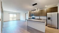 Located at 1851 Brevier Avenue in Cleveland, OH, this well-appointed 2-bedroom, 2-bathroom residence offers a thoughtfully designed single-floor layout with modern finishes throughout. The open-concept living and kitchen area serves as the heart of the home, featuring light wood-tone flooring, recessed lighting, and a striking geometric pendant light fixture above the kitchen island. The kitchen is outfitted with warm bronze flat-panel cabinetry, a white subway tile backsplash, stone-topped counters and island, stainless steel appliances including a refrigerator with ice maker, range, and microwave, and a sleek black-finish faucet. The living area extends toward a sliding glass door that opens to a balcony, allowing natural light to fill the space. Both bedrooms continue the light flooring aesthetic and feature clean white walls, with windows framing outdoor tree views. The spacious primary bedroom includes a generously sized walk-in closet with wire shelving. The bathrooms are finished with contemporary vanities and a soaking tub accented by terrazzo-patterned tile and matte black fixtures. Additional conveniences include in-unit laundry and multiple closets for ample storage throughout.