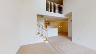 This two-story residence is defined by its dramatic double-height ceiling in the main living area, where a spindle-railed upper-level overlook adds architectural depth and an open, airy atmosphere. The main level flows from the carpeted living space into a dining area illuminated by a classic chandelier, connecting seamlessly to a galley-style kitchen. The kitchen features warm wood cabinetry, ample counter space, tile flooring, and a full suite of white appliances, including a built-in microwave, electric range, refrigerator, and dishwasher. A dedicated laundry closet with a stacked washer and dryer is conveniently accessible directly from the kitchen. A carpeted entry area with a closet provides a practical foyer. Upstairs, the upper level hosts generously sized bedrooms with plush carpet, including one room with vaulted ceiling details and sliding closet doors, and another featuring a large window with views of the surrounding neighborhood. The upper level is served by two full bathrooms: one with a tiled walk-in shower and extended vanity, and another with a soaking tub-shower combination, vanity, and tile flooring throughout.