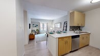 Located in Boston's South End neighborhood, this one-bedroom, one-bathroom residence at 45 E Newton St offers a thoughtfully designed layout across a single floor. The open-concept kitchen and living area forms the heart of the space, creating a seamless flow ideal for both everyday living and entertaining. The kitchen features light wood cabinetry, a gray tile backsplash, white quartz countertops, and a full suite of stainless steel appliances including a range, microwave, dishwasher, and refrigerator. A peninsula with seating for three extends into the living area, doubling as a convenient dining space. The living room is bright and welcoming, with large windows that invite natural light and views of the surrounding neighborhood. Light hardwood-style flooring runs through the main living areas, while plush carpeting adds warmth to the bedroom. The bedroom offers two windows, built-in closet storage, and a calm, neutral palette. The bathroom is finished with wood-look tile flooring, a dark-toned vanity with white countertop, and a full soaking tub with shower. Two hallways connect the rooms, ensuring efficient circulation throughout the residence.