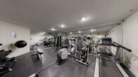 This fitness center is designed to offer a complete workout experience within a single, efficiently organized space. The room features durable rubberized flooring throughout, providing both safety and comfort during exercise. Floor-to-ceiling mirrors line the walls, visually expanding the space while allowing users to monitor their form during workouts.

The cardio section is well-stocked with multiple treadmills, elliptical trainers, and a stationary bike, offering a variety of aerobic exercise options. A multi-station cable machine anchors the strength training area, complemented by a dedicated free weights section that includes a dumbbell rack and a medicine ball. Flat weight benches provide additional versatility for strength routines.

Recessed and flush-mounted ceiling lights ensure the space is evenly and brightly illuminated throughout. Informational signage is posted throughout the room, and a wall clock helps users track their workout sessions. The facility includes a private restroom with a vanity, mirror, and all essential amenities for post-workout convenience.

The overall layout is clean and functional, with equipment arranged to maximize usable floor space and allow for comfortable movement between stations. The neutral color palette of white walls and gray tones lends the space a modern, professional atmosphere.