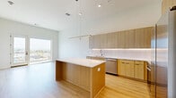Located in Nashville, TN, this contemporary one-bedroom, one-bathroom unit offers a thoughtfully designed open-concept layout with a clean, modern aesthetic throughout. The kitchen is a standout feature, showcasing light wood cabinetry with under-cabinet LED lighting, crisp white quartz countertops, a subway-tile backsplash, and a full suite of stainless steel appliances including a range, microwave, and French door refrigerator. A central island provides additional prep and dining space, while soaring ceilings lend an airy, expansive feel to the combined kitchen and living area. Light wood-tone flooring runs throughout the space, enhancing the bright and welcoming atmosphere. The generously sized primary bedroom features large floor-to-ceiling windows and direct balcony access, flooding the room with natural light and offering sweeping views of the Nashville skyline and surrounding hills. Additional rooms throughout the unit share this same access to natural light and outdoor views via oversized windows and sliding glass doors. The bathroom is finished with modern tilework, a walk-in shower with subway tile surround, and contemporary wood-toned vanity cabinetry. A dedicated closet and in-unit laundry add everyday convenience to this well-appointed Nashville residence.