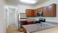 This single-floor residence offers a thoughtfully designed layout that balances functionality and comfort throughout its living spaces. The kitchen serves as a central highlight, featuring rich warm-toned wood cabinetry with ample upper and lower storage, granite-style countertops, and a full suite of stainless steel appliances including a gas range, over-the-range microwave, and refrigerator. A peninsula counter with a built-in sink adds additional prep space and creates a natural flow into the adjacent areas. Light wood-style flooring runs through the kitchen and living spaces, adding warmth and continuity. The living area is bright and open, benefiting from natural light through large windows fitted with blinds, a ceiling fan with light fixture, and a door providing direct access to the outdoors. The bedrooms are carpeted for comfort, offering neutral tones and windows that allow for natural light. Additional rooms provide versatile space suitable for various uses. A dedicated laundry area houses a full-size side-by-side washer and dryer, adding everyday convenience. The overall ambiance is clean, functional, and move-in ready, with a consistent neutral color palette and practical finishes throughout.