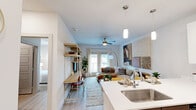 Located in Austin, TX, this thoughtfully designed one-bedroom, one-bathroom residence offers an efficient and stylish layout across a single floor. The open-concept kitchen and living area forms the heart of the home, where the kitchen stands out with crisp white upper cabinetry, warm wood-toned lower cabinets, a classic subway tile backsplash, quartz countertops, stainless steel appliances, and pendant lighting over a functional breakfast bar. Light wood-style flooring flows throughout, adding warmth and visual continuity. The living room is bright and welcoming, with large windows and French doors that invite natural light and connect the space to the outdoors. A ceiling fan overhead adds comfort and practicality. The bedroom is a serene retreat, featuring a padded wall-panel headboard, a ceiling fan, and a window dressed with sheer curtains that diffuse natural light softly across the room. The bathroom is clean and well-appointed, offering a soaking tub with shower combination, dark wood cabinetry, a white quartz vanity countertop, and tile flooring. A dedicated closet and hallway round out the layout, ensuring practical storage and smooth circulation throughout this well-organized Austin residence.