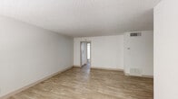This single-floor unit offers a bright, well-organized layout with a cohesive neutral color palette throughout. Light wood-style flooring runs continuously across the main living areas and bedrooms, providing a warm and consistent aesthetic. The ceilings feature a classic textured finish, adding subtle dimension to each room.

The open living area is airy and versatile, with clean white walls, a ceiling fan, and a large window fitted with horizontal blinds that allows natural light to fill the space. A dedicated entry door with an adjacent window contributes to the welcoming feel of the main area. Overhead ventilation is present, ensuring comfort year-round.

The kitchen is efficiently designed with gray lower cabinetry, white upper cabinets, light quartz-style countertops, and a stainless steel refrigerator. A window above the counter brings in natural light, and the space accommodates a full range with coil burners, making it a fully functional cooking environment.

The bedroom is a quiet, well-proportioned room featuring a wide window with vertical blinds that offers ample natural light and privacy. Additional rooms visible in the floor plan provide flexible use of space.

The bathroom is clean and straightforward, featuring wood-style tile flooring, a full soaking tub with a showerhead, a toilet, and a vanity with storage — all finished in bright white tones for a fresh, hygienic feel.