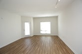 This single-floor residence is designed with an open-concept layout that seamlessly connects the kitchen and living areas. The main living space features warm-toned hardwood-style flooring and crisp white walls, creating a bright and airy atmosphere. Track lighting runs along the ceiling, providing functional illumination, while a large window with blinds allows natural light to filter in.

The kitchen is a standout feature, centered around a curved island with a quartz-style countertop, an undermount double sink, and pendant lighting overhead. White cabinetry lines the walls alongside stainless steel appliances, including a refrigerator, microwave, and electric range. The kitchen flows directly into the open living area, making the space ideal for entertaining.

The bedrooms are carpeted and well-proportioned, each equipped with ceiling fans and windows with blinds that provide natural light. The primary bedroom connects to a full bathroom featuring a double-sink vanity with grey countertops, ample cabinetry, and an adjacent walk-in closet with wire shelving. A compact half bathroom with a pedestal sink and hardwood-style flooring serves as an additional convenience. The overall design is clean, modern, and highly functional.