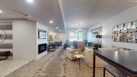 Located at 426 S Jefferson Ave in Springfield, Missouri, this single-floor amenity lounge is designed with a modern, upscale aesthetic that balances comfort and functionality. The main lounge area serves as the centerpiece of the space, featuring plush neutral-toned sofas arranged around a sleek linear fireplace set into a light wood surround. A wall-mounted flat-screen TV anchors the living area, while statement sputnik chandeliers overhead add a bold, contemporary flair. Patterned area rugs in warm earth tones define the seating zones and complement the neutral walls and recessed lighting throughout.

A built-in bar-height table with leather-and-gold bar stools provides a casual gathering spot, positioned beneath additional sputnik pendant lights. Gold-accented side tables and decorative mirrors add refined detail throughout the lounge. Adjacent to the main seating area, a dedicated dining section features booth-style and chair seating arranged around tables, framed by circular wall mirrors and wall sconces.

A sleek kitchenette serves the space with dark granite countertops, warm yellow cabinetry, a brass faucet, and a glossy white subway tile backsplash, along with open shelving and appliances. A compact business area with a wall-mounted TV, printer, and workstation desk rounds out the functionality of this well-appointed communal space.