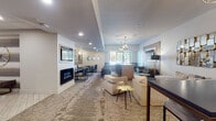 Located at 426 S Jefferson Ave in Springfield, Missouri, this single-floor amenity lounge is designed with a modern, upscale aesthetic that balances comfort and functionality. The main lounge area serves as the centerpiece of the space, featuring plush neutral-toned sofas arranged around a sleek linear fireplace set into a light wood surround. A wall-mounted flat-screen TV anchors the living area, while statement sputnik chandeliers overhead add a bold, contemporary flair. Patterned area rugs in warm earth tones define the seating zones and complement the neutral walls and recessed lighting throughout.

A built-in bar-height table with leather-and-gold bar stools provides a casual gathering spot, positioned beneath additional sputnik pendant lights. Gold-accented side tables and decorative mirrors add refined detail throughout the lounge. Adjacent to the main seating area, a dedicated dining section features booth-style and chair seating arranged around tables, framed by circular wall mirrors and wall sconces.

A sleek kitchenette serves the space with dark granite countertops, warm yellow cabinetry, a brass faucet, and a glossy white subway tile backsplash, along with open shelving and appliances. A compact business area with a wall-mounted TV, printer, and workstation desk rounds out the functionality of this well-appointed communal space.